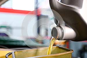 Close-up shot of pouring oil into the engine compartment Auto mechanic in car repair shop is pouring golden yellow engine oil in
