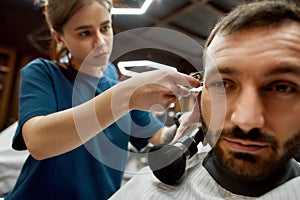 Close up shot of a professional barber girl or female hairdresser working with hair clipper, making trendy haircut for a