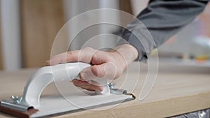 Close up shot of a professional carpenter sanding a wood board with sanding paper in a workshop.