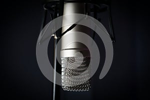 Close-up shot of a professional fixed microphone used for studio recordings in the dark background.