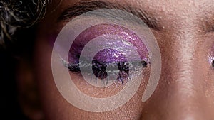 Close up shot on purple glowing wet makup eye of beautiful African fashion model