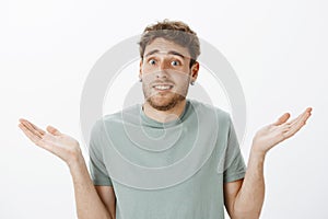 Close-up shot of questioned awkward handsome male in earrings, shrugging and spreading palms cluelessly, being unaware