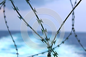 Close up shot of razor wire on a ship with a blurred ship\'s wake and blue ocean in the background