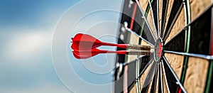 Close up shot red darts arrows in the target of dartboard center on dark blue sky background. Business target or goal