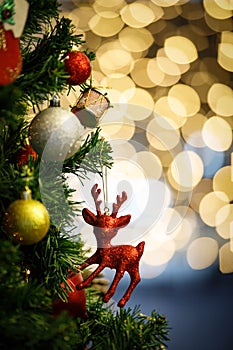 Close up shot of red glossy Christmas eve decor reindeer model hanging decorating on green Xmas pine tree branch with sphere balls