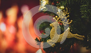 Close up shot of red glossy Christmas eve decor reindeer model hanging decorating on green Xmas pine tree branch with sphere balls