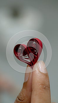 A close-up shot of a red quilled paper heart held between two fingers