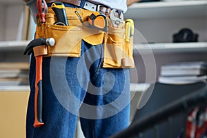Close up shot of repairman wearing a toolbelt, getting ready for work, standing indoors