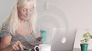 Close up shot of retired old woman grandmother count a bundle of money dollars while seating at the laptop at home