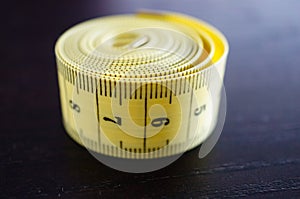Close up shot of a rolled yellow measuring tape in centimeters on a wooden surface