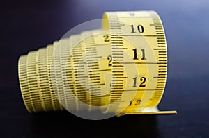 Close up shot of a rolled yellow measuring tape in centimeters on a wooden surface