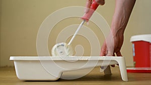 Close-up shot of a roller picking up paint from a plastic tub. Footage. Home renovation and renovation concept.