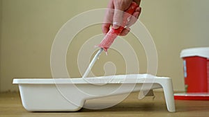 Close-up shot of a roller picking up paint from a plastic tub. Footage. Home renovation and renovation concept.