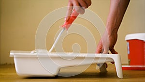 Close-up shot of a roller picking up paint from a plastic tub. Home renovation and renovation concept.