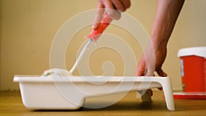 Close-up shot of a roller picking up paint from a plastic tub. Home renovation and renovation concept.