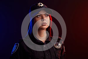 Close-up shot of serious female police officer posing for the camera against a black background with red and blue