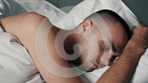 Close up shot of sleepy Caucasian man waking up in the morning, taking a smartphone from the bedside table and turning