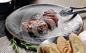 Close up shot sliced medium rare steak served on plate with cutlery and bowl with fresh baked bread