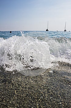 Close up shot of small breaking waves on the beach side. Lovely small surge with sand and boats, blue ocean water and boats in the