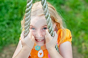 Close up shot of smiley pretty blonde girl`s face while clinging to a rope. Focus on eyes, blurry background