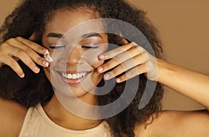 Close up shot of smiling dark skinned woman with curly afro hair applying face cream