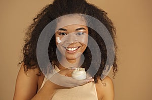 Close up shot of smiling dark skinned woman with curly afro hair applying face cream