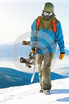 Close up shot of a snowboarder walking at the top of a mountain at golden hour