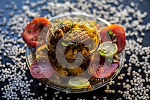 Close up shot of spicy tasty sabudana khichdi or sago ball khichdi along with some sliced tomatoes, some cut lemons in a glass pla