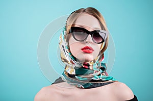 Close up shot of stylish young woman in sunglasses and you colored shawl, headscarf, scarf against blue background. Beautiful fema