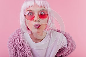 Close-up shot of surprised young lady in peruke posing with kissing face expression in studio with