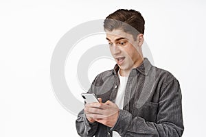 Close up shot of surprised young man staring at phone in awe, checking out awesome news on smartphone, receive