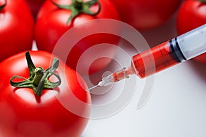 Close-up shot of a syringe injecting a red liquid to fresh red tomatoes.