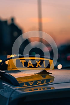 Close-up shot of a taxi sign in the warm colours of sunset with bokeh lights in the background