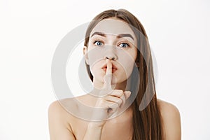 Close-up shot of tender and sensual feminine brunette female posing naked showing shhh gesture asking keep secret of