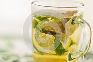 Close up shot of a transparent cup with brewing tea bag in it, lemon and mint. Refreshment