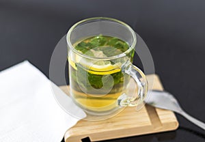 Close up shot of a transparent cup with brewing tea bag in it, lemon and mint. Refreshment