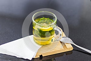 Close up shot of a transparent cup with brewing tea bag in it, lemon and mint. Refreshment