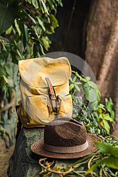 close-up shot of vintage yellow backpack and straw hat on rock in jungle