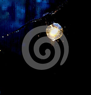 Close-up shot of a wet illuminated garden lightbulb hanging outdoors