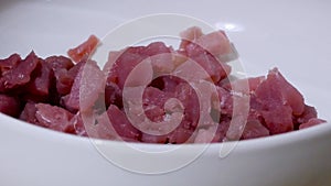 close-up shot of white bowl with cut raw red tuna cubes inside to eat raw or serve