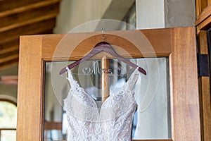 Close up shot of a white lace wedding dress hanging from the door