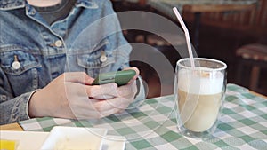 Close up shot of a woman in denim jacket uses smartphone sitting in a restaurant.