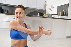 Close up shot of woman doing workout from home, warm-up stretching hands, does fitness exercises in blue sportsbra and