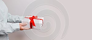 Close up shot of woman hands holding surprise gift package box with red satin bow on pink pastel background with