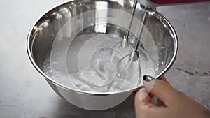 Close up shot of woman hands mixing white egg cream in bowl using motor mixer.