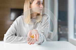 Close-up shot of a woman`s hand holding a few yellow pills