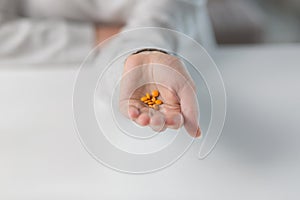 Close-up shot of a woman`s hand holding a few yellow pills