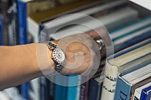 Close up shot of a woman's hand reaching out for the book in the bookshelf. Concept