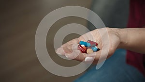 Close up shot of a woman sitting on the couch and holding many colorful pills in her hand, showing them to the camera