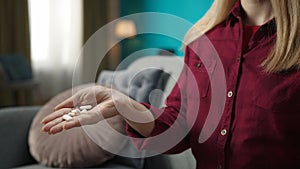 Close up shot of a woman sitting on the sofa holding a pile of pills in her open hand